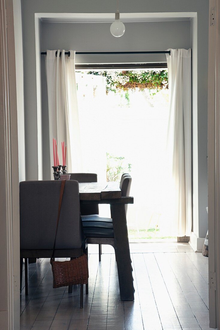 Dining area with rustic table lit from behind by open French windows leading to garden