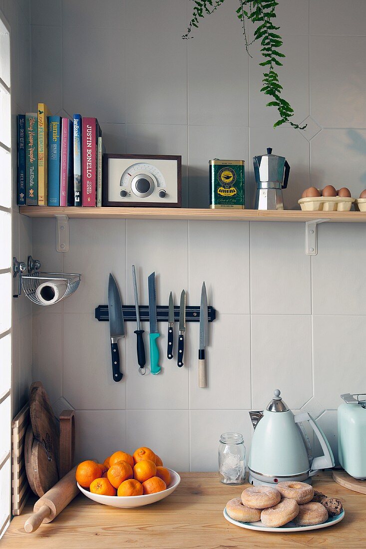 Stillleben in Küchenecke mit Regal für Kochbücher, Radio und Küchenutensilien über einem Messerbord