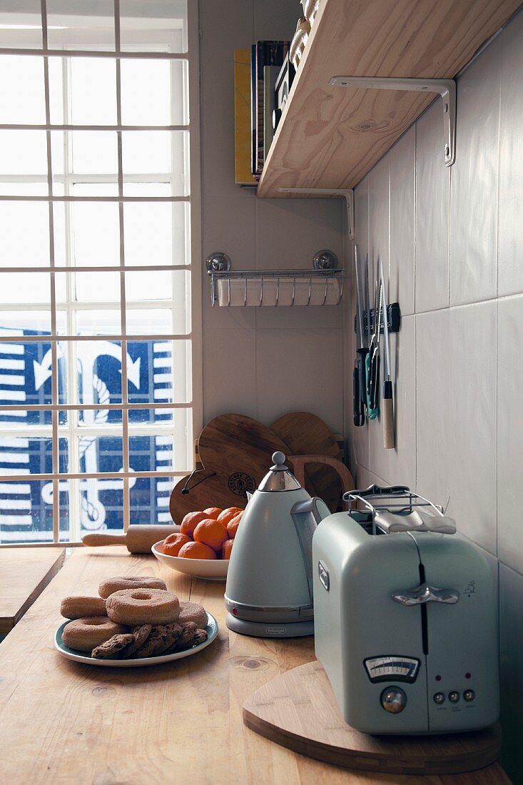 Toaster und Kanne im Vintagestil auf Küchenarbeitsfläche vor einem Fenster mit Blick auf maritimes Ankermotiv