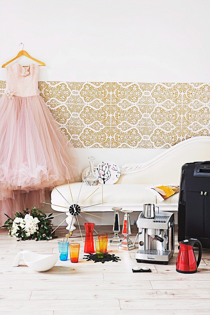 Geschenkideen zur Hochzeit - Espressomaschine und bunte Gläser auf Holzboden vor Vintage Chaiselongue, daneben Brautkleid auf Kleiderbügel an Wand