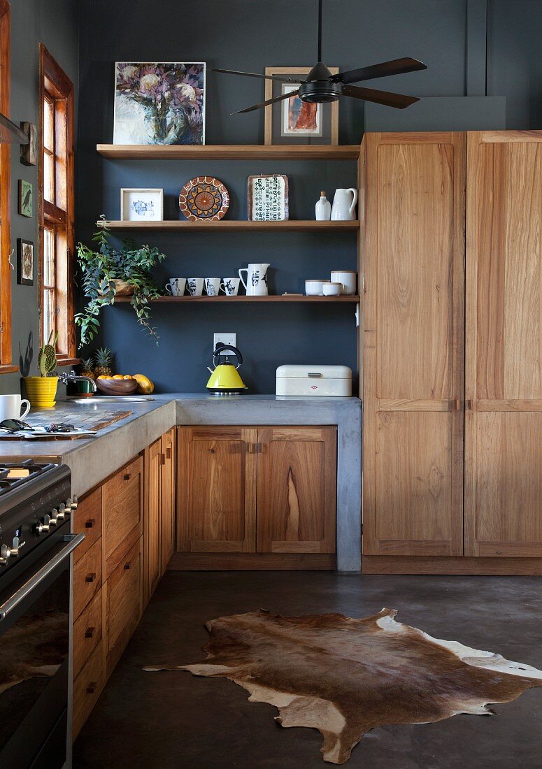 Gemauerte Küchenzeile und Massivholz Schrankfronten in offener Küche mit schwarz getönter Wand, Tierfell auf Estrichboden