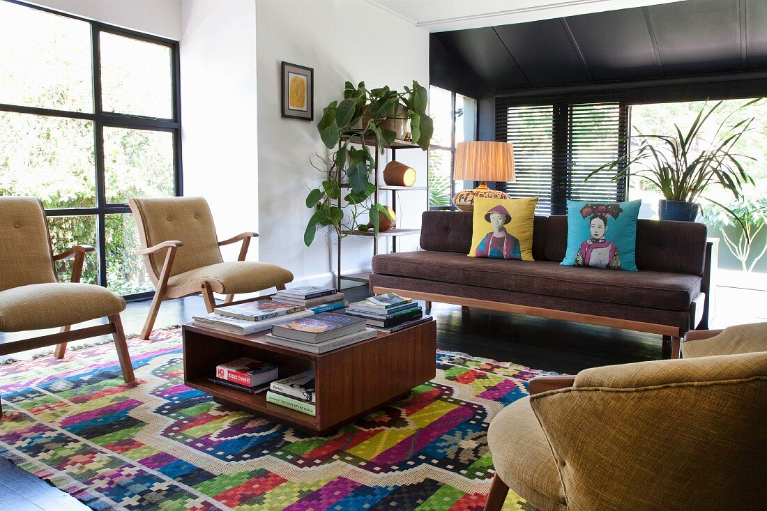Sessel und Sitzbank um Coffee Table im Retrostil auf bunt gemustertem Teppich, in modernem, offenem Wohnraum