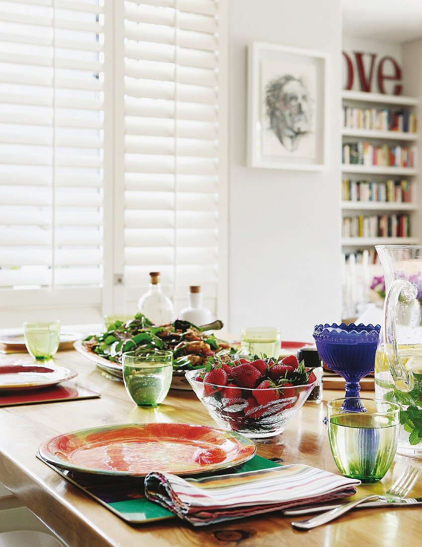 Farbig gemusterte Gedecke und gefüllte Wassergläser, Glasschale mit frischen Erdbeeren auf Tisch