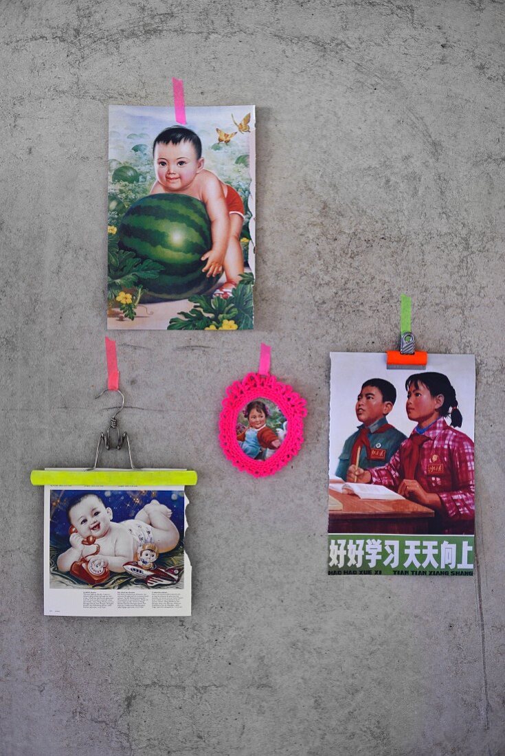 An Betonwand geklebte Kindermotivdrucke, Klemme und Kleiderbügel mit neonfarbenem Streifen, gehäkelter Rahmen in Pink um nostalgisches Kinderbild