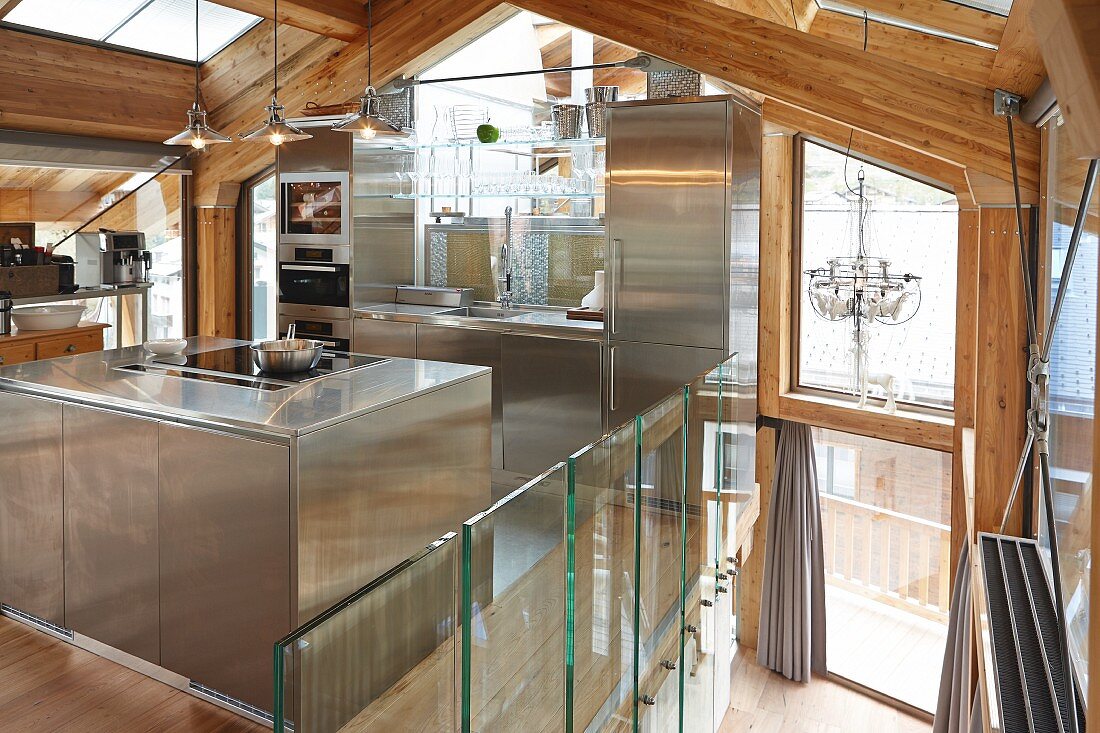 Designer-Einbauküche aus Edelstahl in modernem Chalet mit sichtbarer Holz-Dachkonstruktion und Glasfronten
