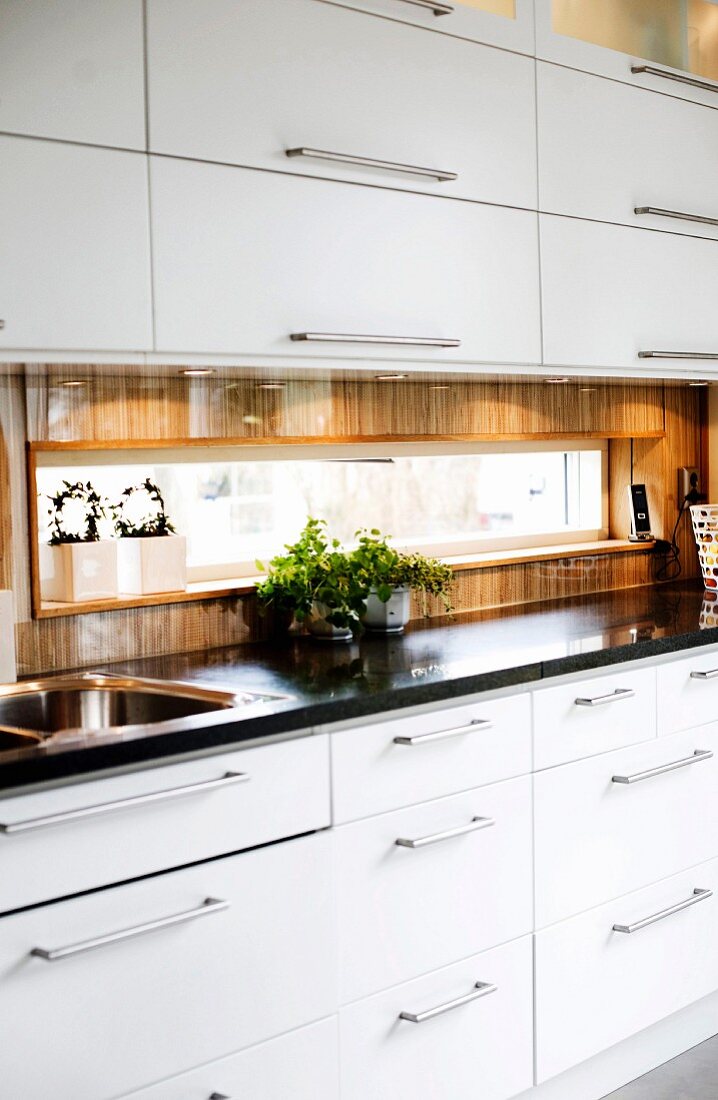 Modern fitted kitchen with white fronts and stainless steel handles; ribbon window with view in splashback area