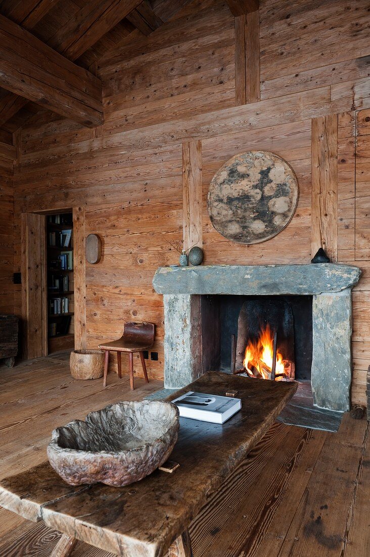 Rough bowl made of natural material on rustic wooden coffee table in front of open fire in cabin interior