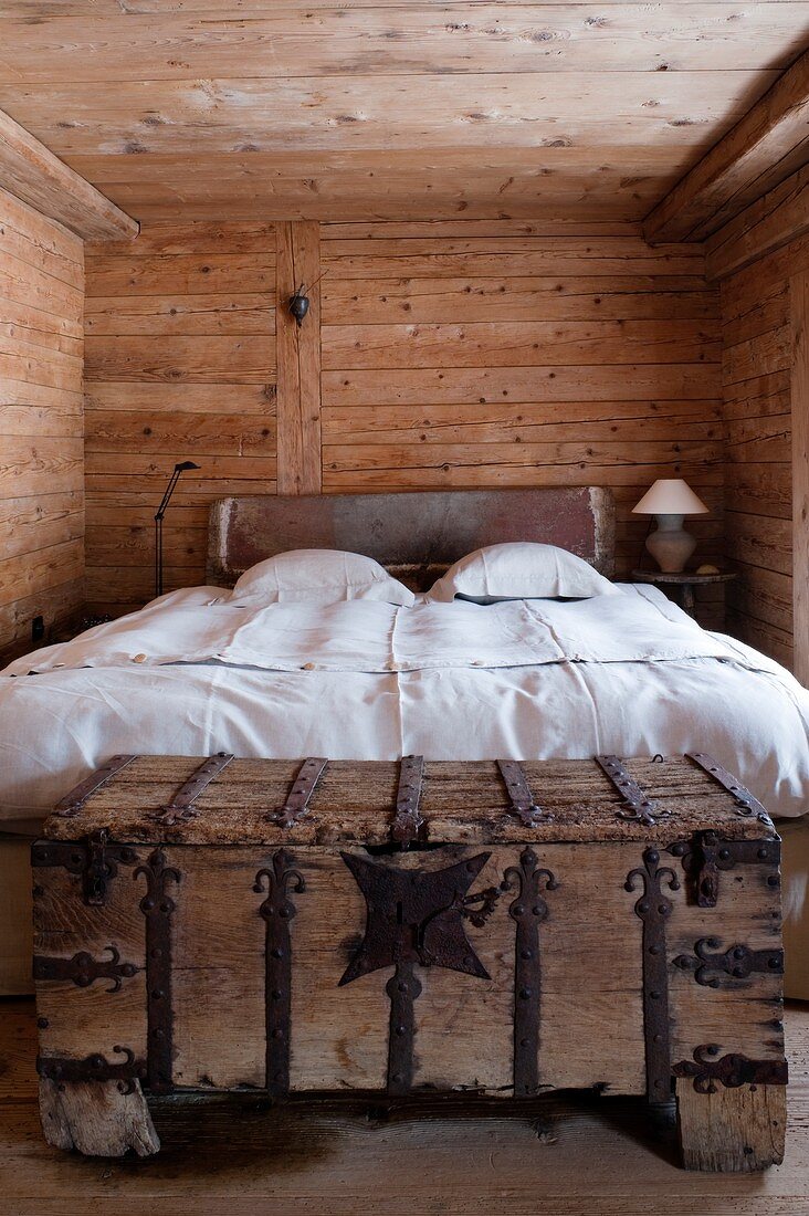 Schlichtes Hütten Schlafzimmer - Doppelbett mit weisser Bettwäsche, an Bettende rustikale Holztruhe mit schmiedeeisernem Beschlag