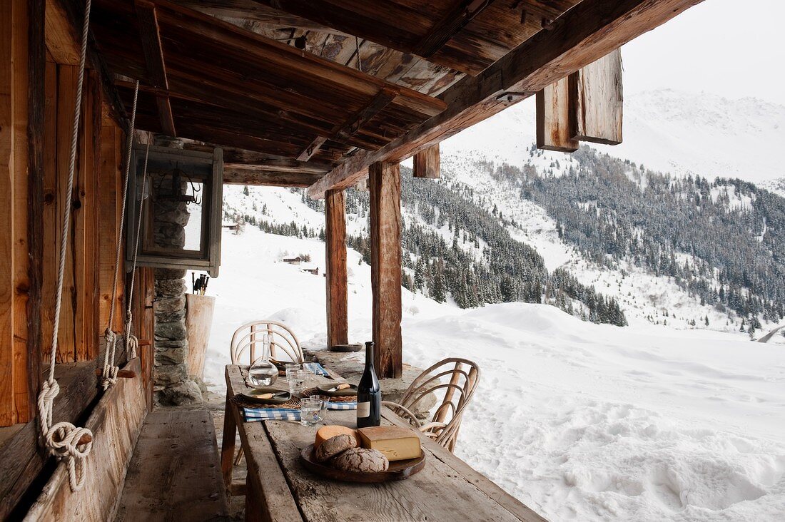 Brotzeit auf rustikalem Holztisch vor Hütte, Blick auf winterliche Berglandschaft