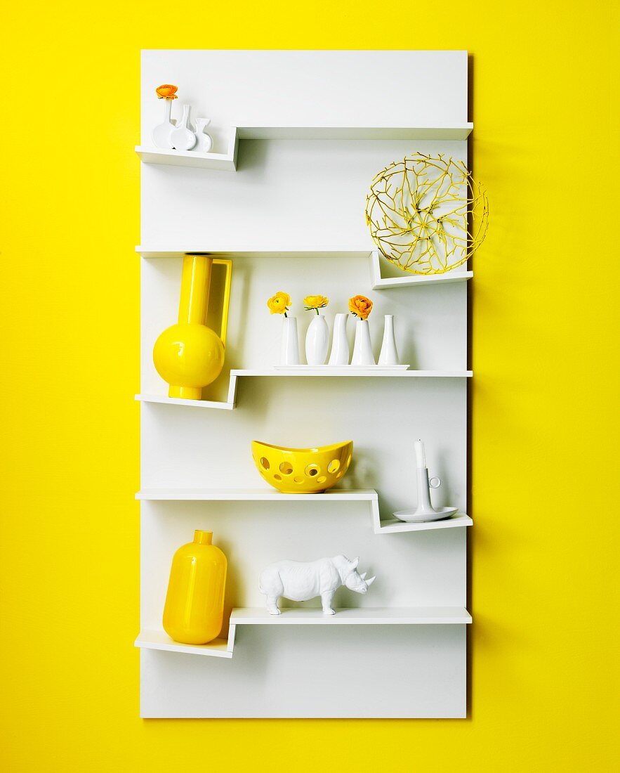 Weisses Hängeboard mit Deko-Objekten auf Zickzack-Fächern an gelber Wand