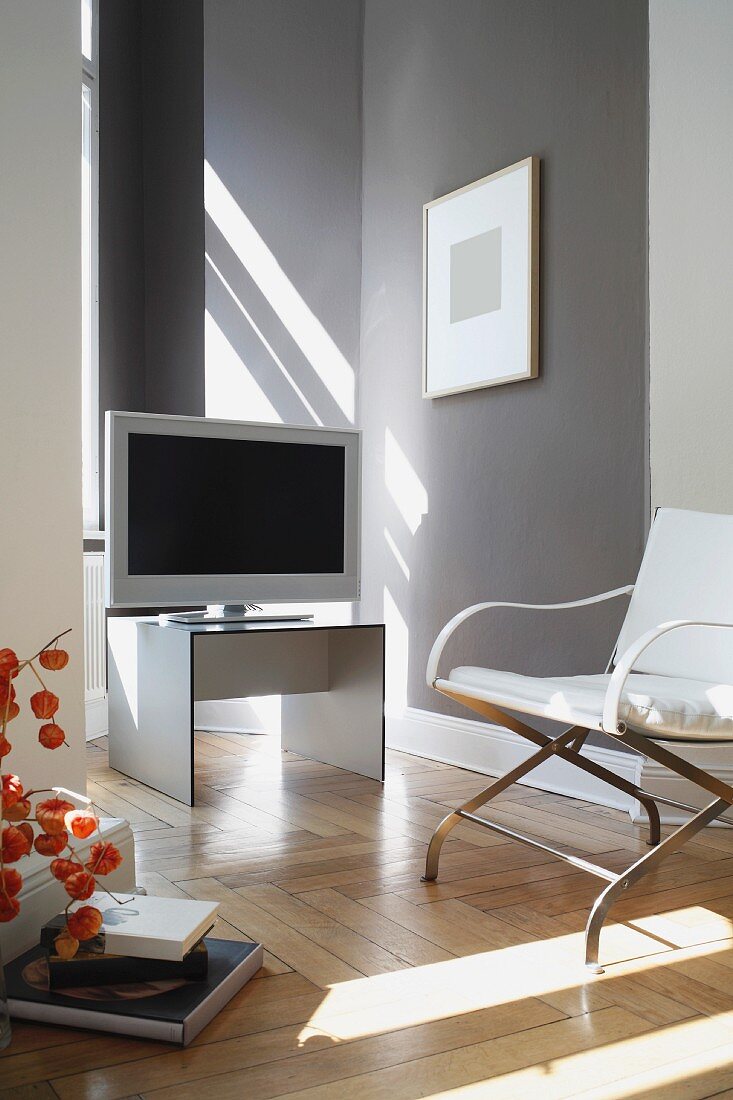 Flachbildschirm und Sessel mit Metallgestell in modernem Wohnzimmer mit hellgrau getönter Wand