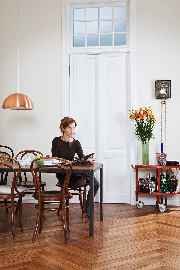 Junge Frau mit Kaffee und Zeitung an modernem Esstisch mit Thonetstühlen in grosszügiger Altbauwohnung