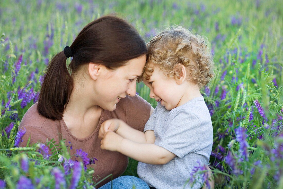 A woman and a young boy sitting face to face in a field