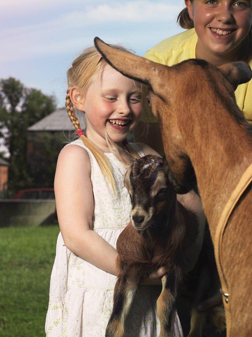 Zwei Mädchen mit Ziege und Zicklein auf dem Bauernhof