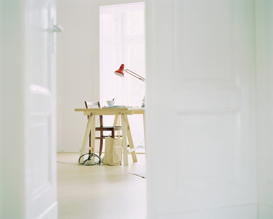 Blick durch offene Tür auf Schreibtisch mit Holzböcken im weissen Raum