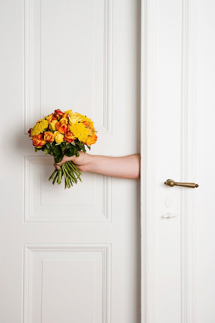 Hand mit gelbem Blumenstrauss in Türspalt