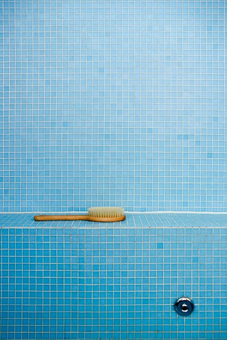 Massagebürste auf Ablage in Badezimmer mit blauen Mosaikfliesen