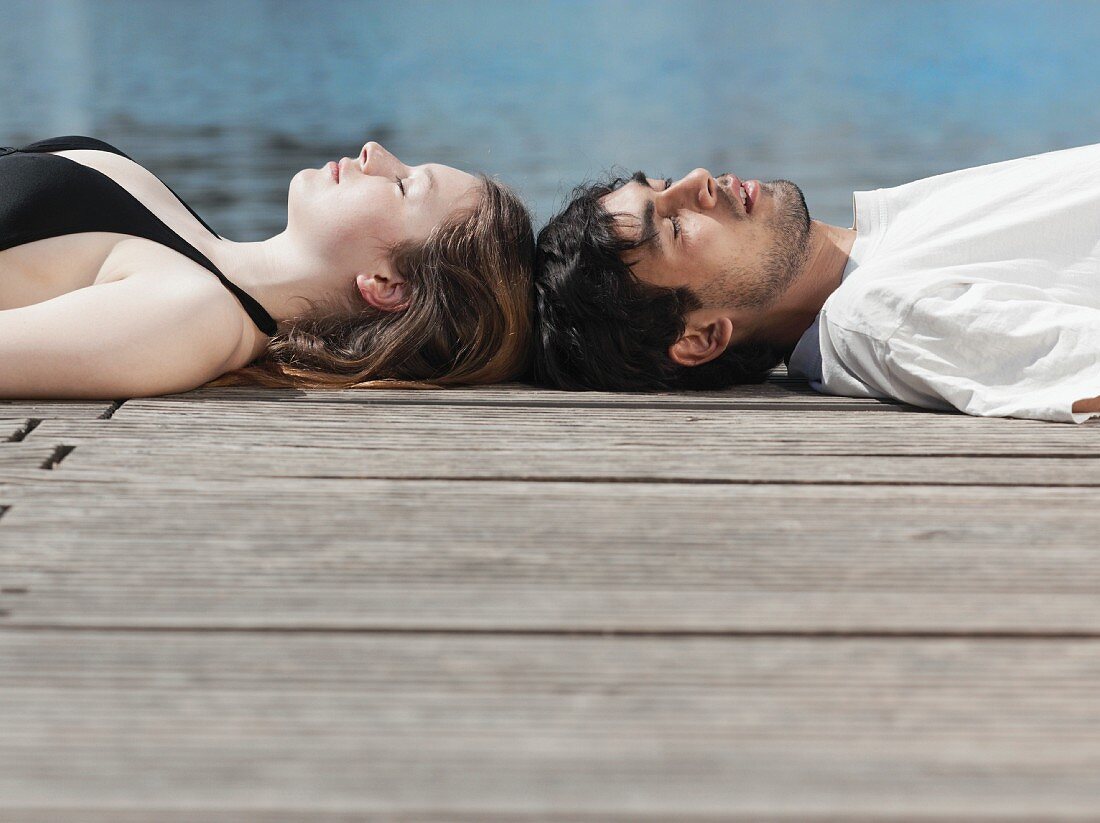 A young couple lying on a jetty head to head