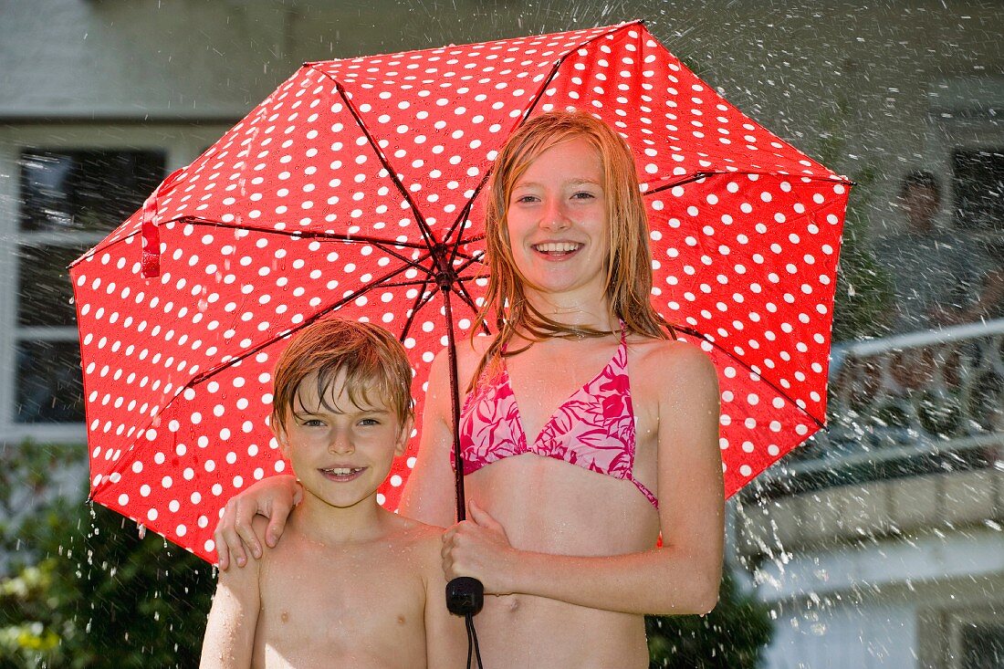 Zwei Kinder in Badekleidung unter einem gepunkteten Regenschirm