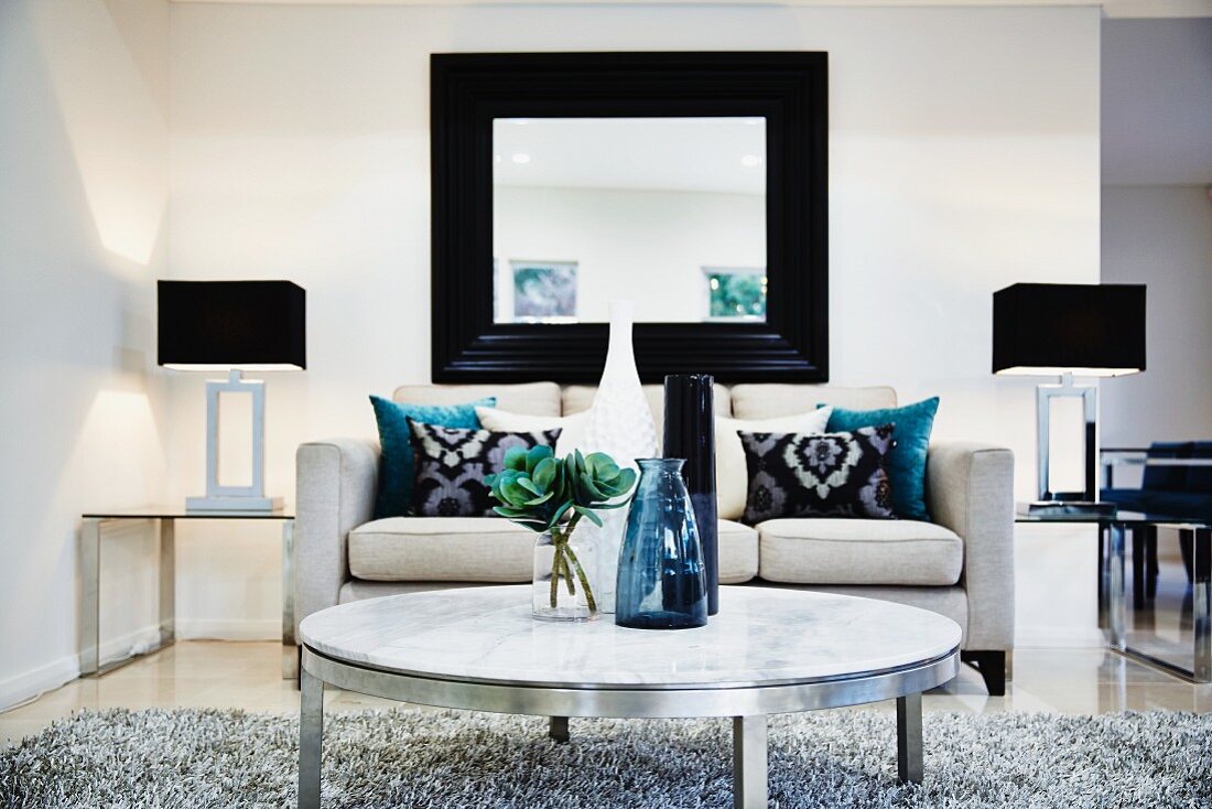 Modernes Wohnzimmer mit Sofa, Wandspiegel, Metalltisch, Teppich und Beistelltischchen aus Glas mit Lampen