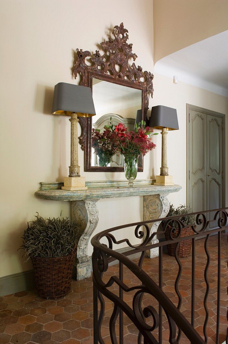 Elegant, stone console table, ornate mirror and table lamps in terracotta-tiles hallway in historical, French country house