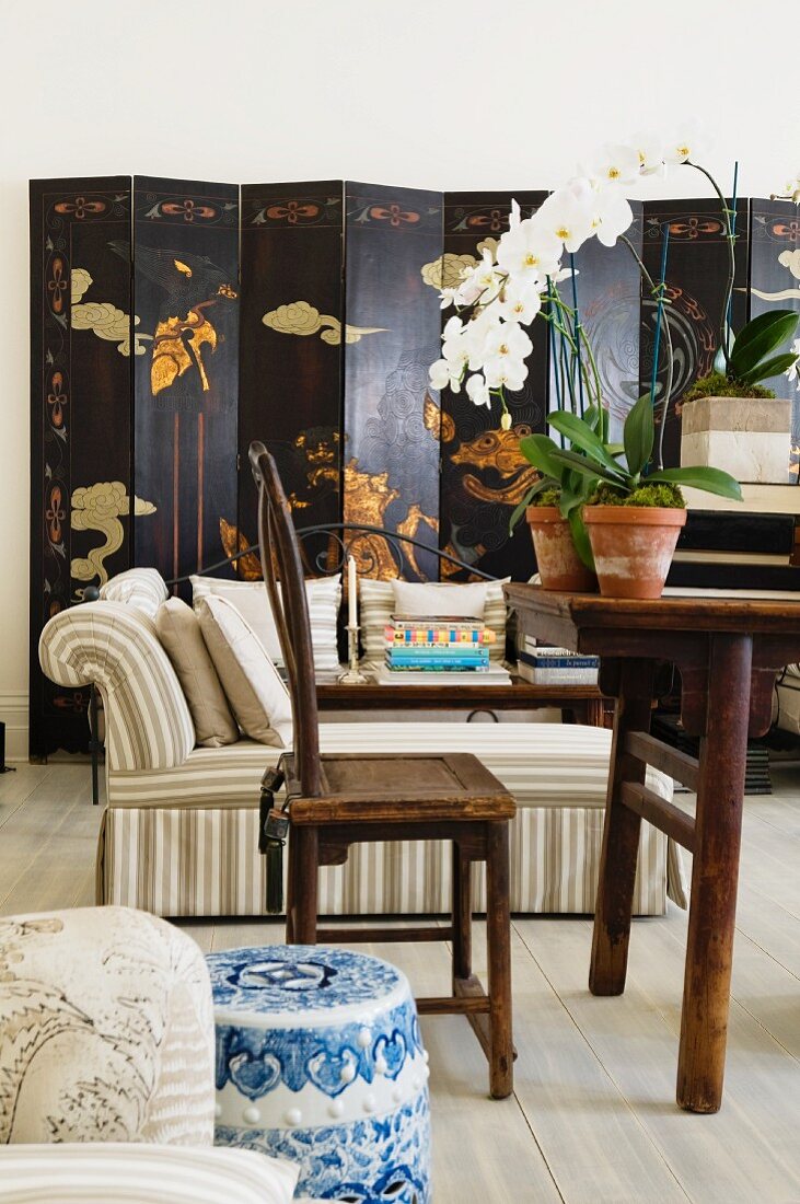 Traditionelles Wohnzimmer mit asiatischem Paravent, beige-weiß gestreiften Polstermöbeln und antikem Holzstuhl mit Tisch