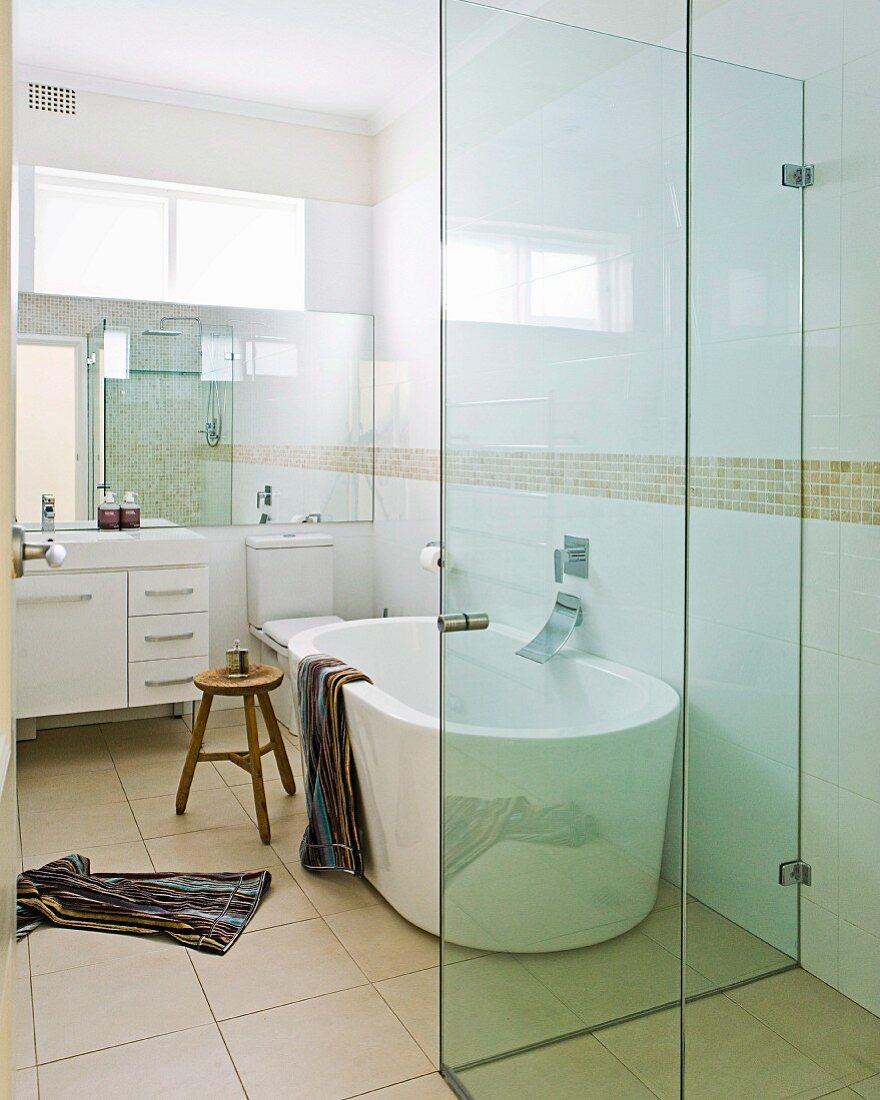 Blick durch offene Tür in Designerbad - verglaster Duschbereich vor Badewanne auf sandfarbenen Bodenfliesen