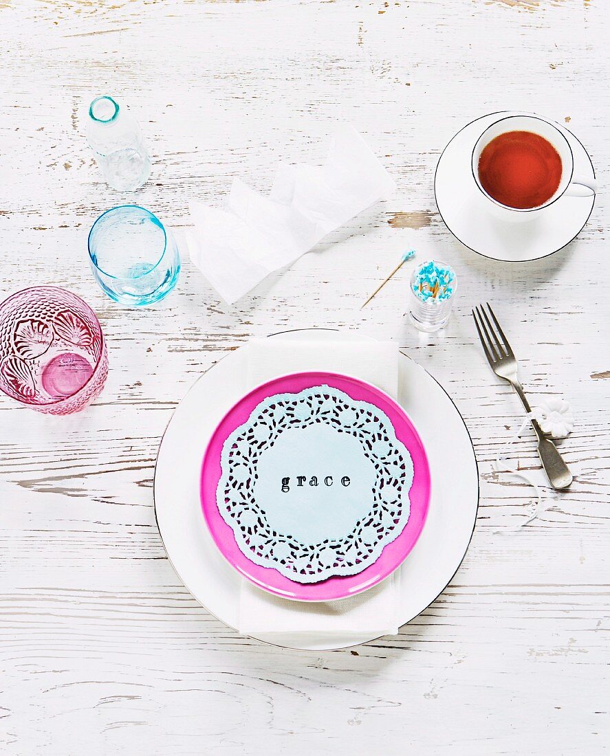 Hand-crafted table decorations with name printed on lace doily; set of plates, fork and teacup on white, shabby chic table