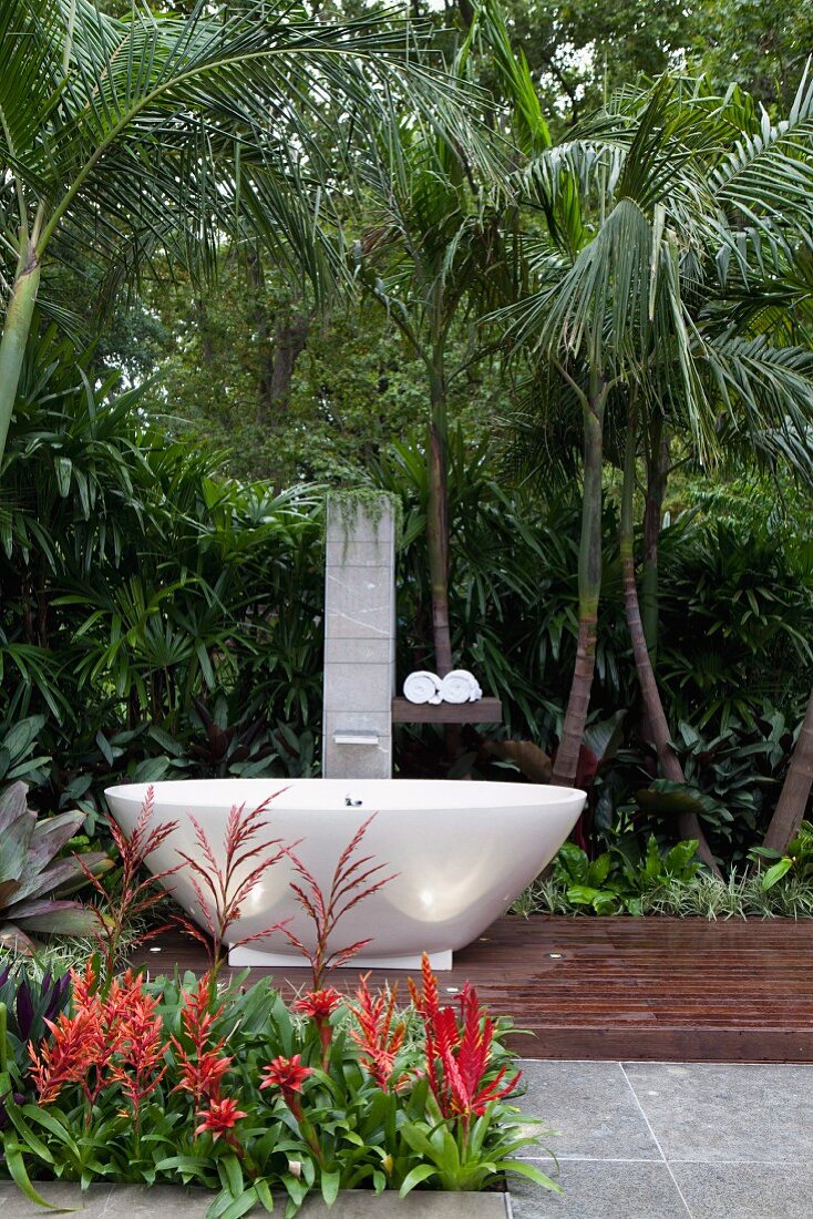 Free-standing, oval designer bathtub on wooden platform in front of tropical planting