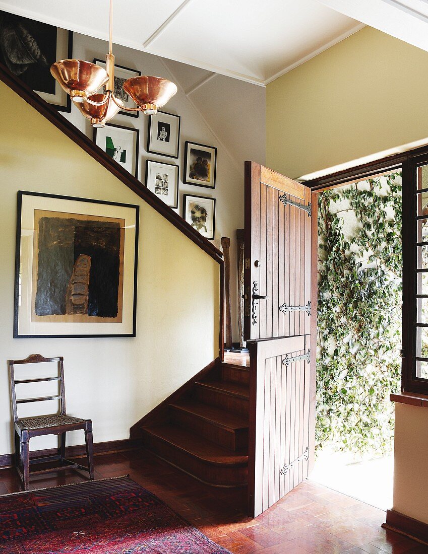 Traditioneller Vorraum mit Holztreppe neben offener Haustür und Blick auf berankte Hausfassade