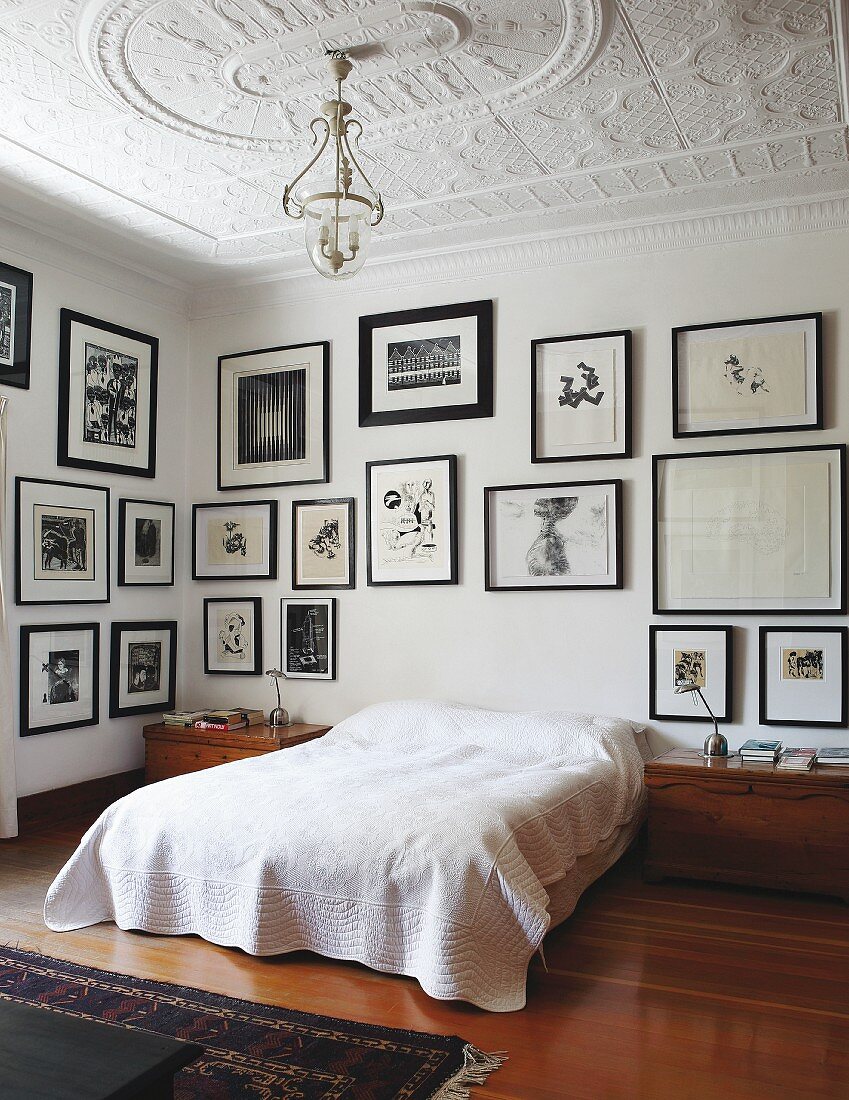 Doppelbett mit weisser Tagesdecke vor Wand mit gerahmter Bildersammlung in traditionellem Schlafzimmer mit Stuckdecke