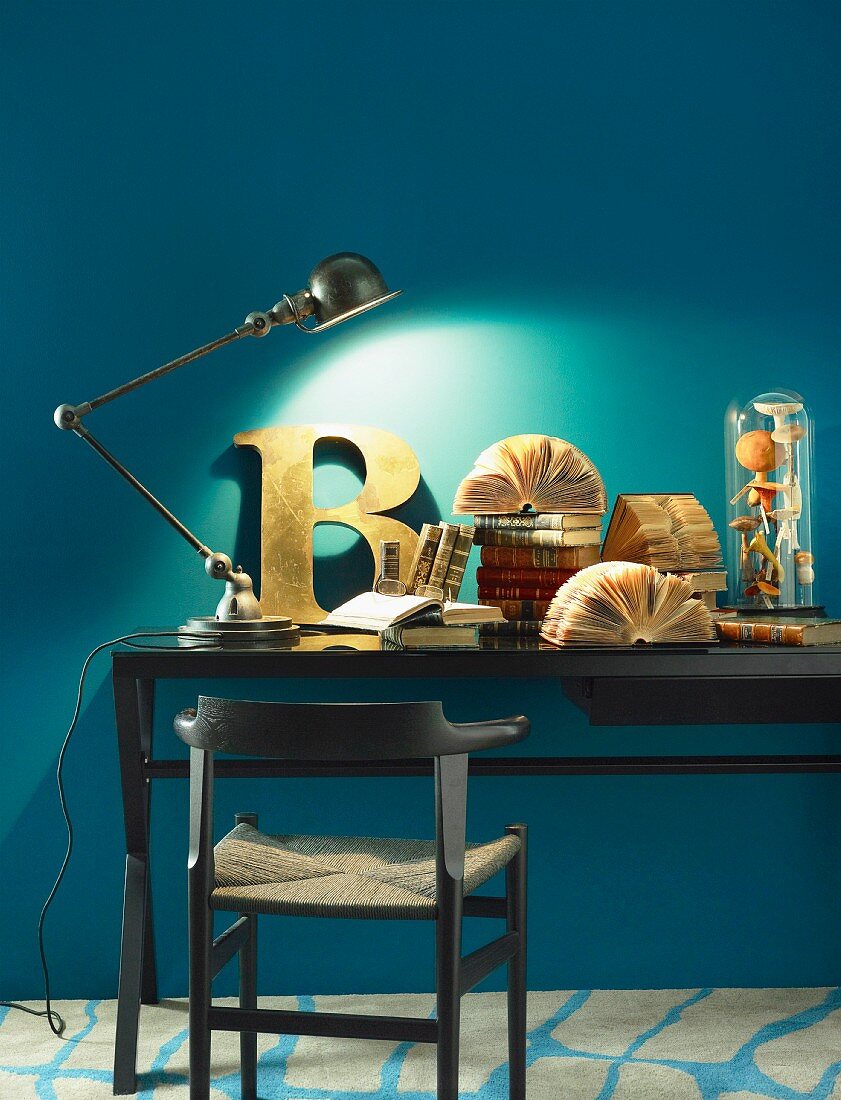 Gelenk-Tischleuchte, Deko-Buchstabe und antike Bücher auf einem Schreibtisch vor blauer Wand