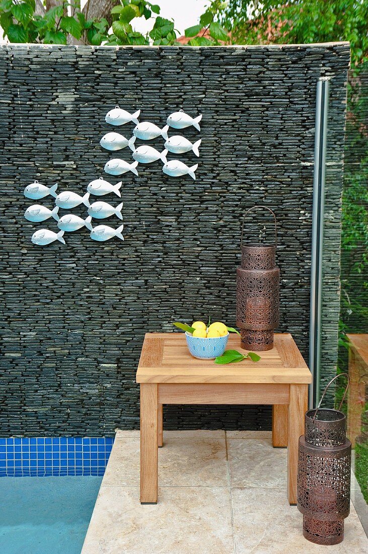 Screen of stacked stones with fish ornaments next to pool