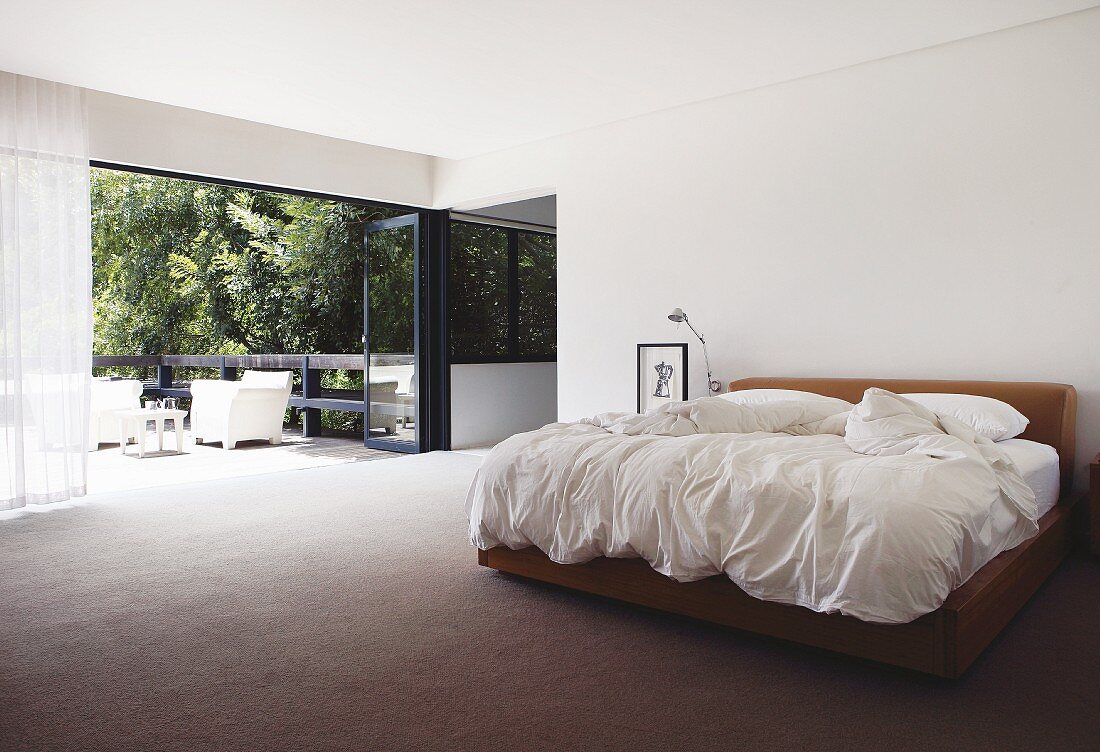 Minimalistisches Schlafzimmer mit Doppelbett und offene Terrassen Falttür mit Gartenblick