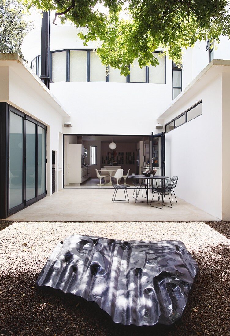 Skulptur aus Metall auf Boden vor Terrasse mit Outdoormöbeln im Patio eines zeitgenössischen Wohnhauses