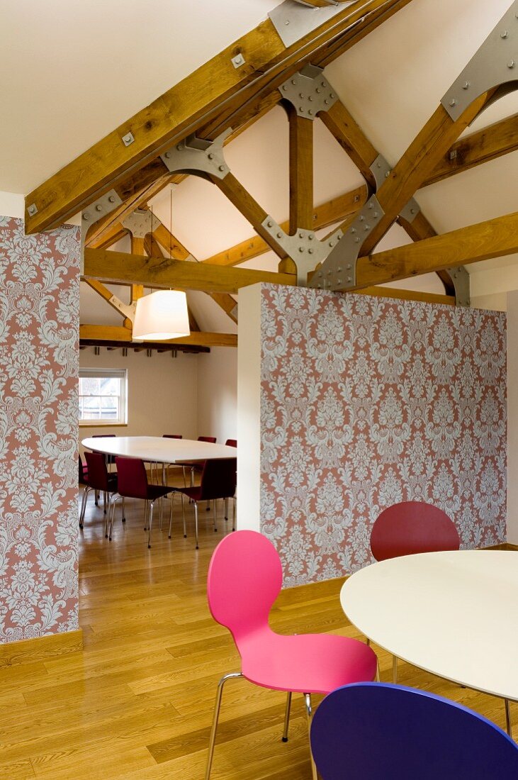 Colourful, retro shell chairs around white table; partition covered in patterned wallpaper and conference table and chairs in background