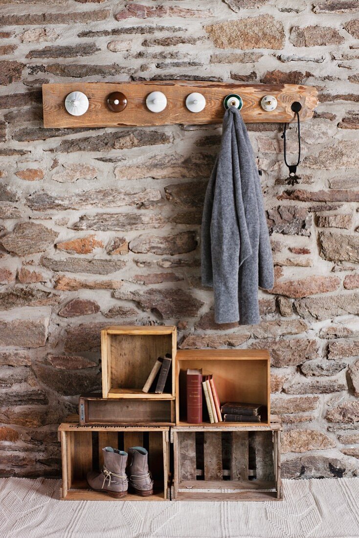 Rustic DIY cloakroom in room with stone wall; coat pegs made from old china lids and old wooden crates on floor as storage