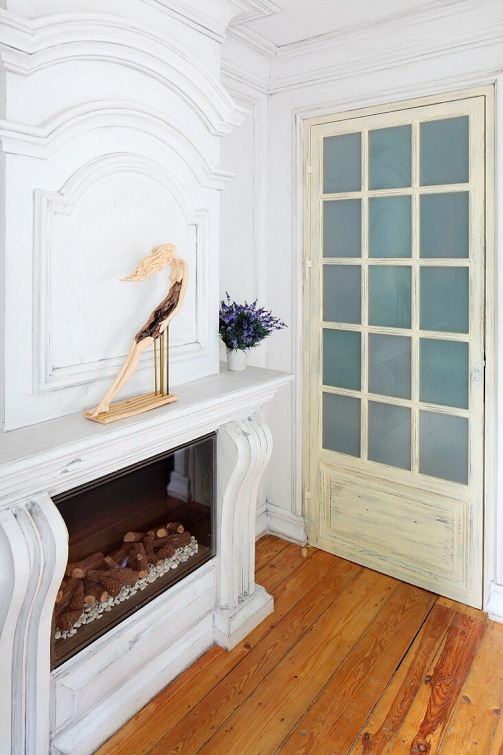 Fireplace with custom, wooden surround painted white and lattice door to one side in traditional interior with rustic ambiance