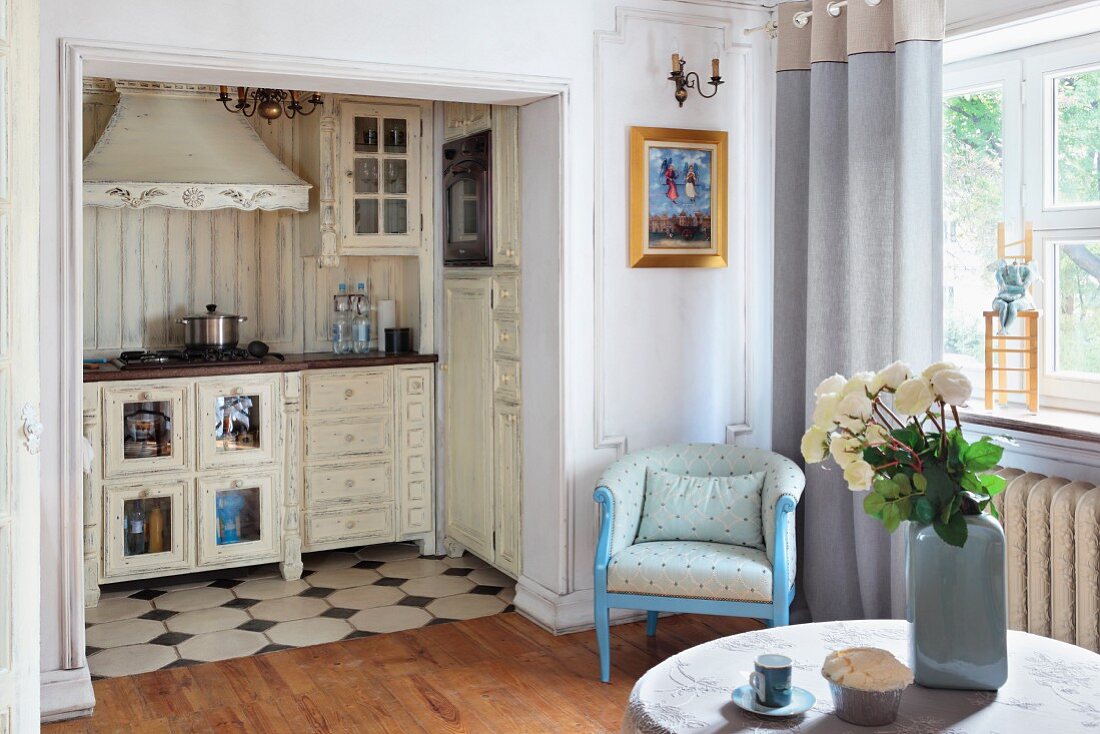 Weisser Rosenstrauss auf Tisch in Wohnraum, im Hintergrund offener Durchgang und Blick auf Kochecke im Shabby Stil