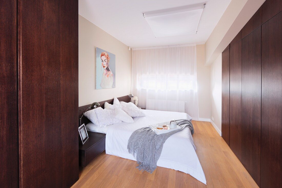 Elegant bedroom with contemporary ambiance; double bed with white covers and flat-fronted, dark wood fitted wardrobes