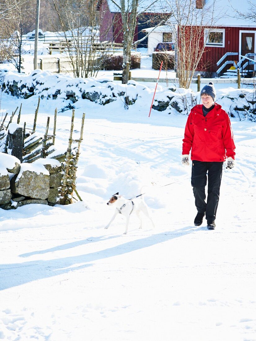 Frau mit Hund auf verschneiter Strasse in Skandinavien