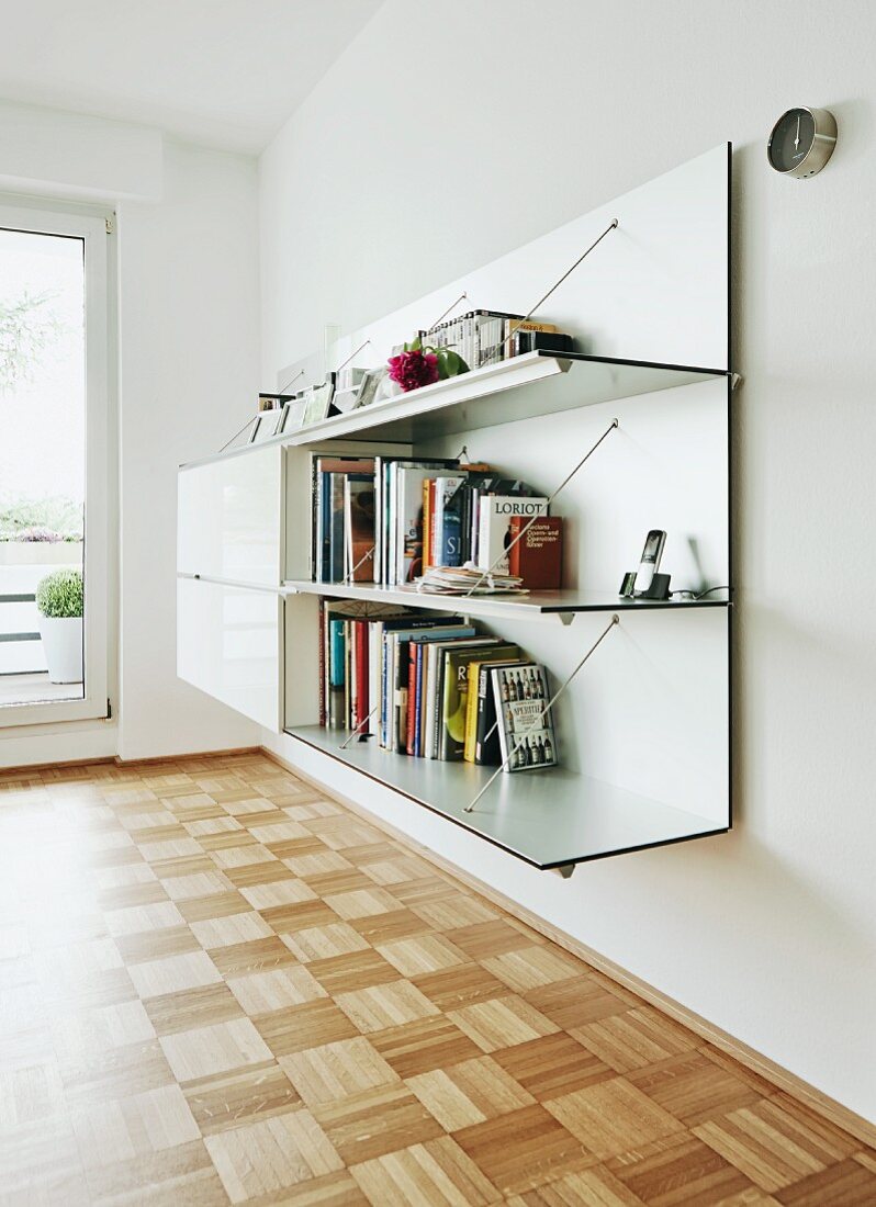 Wall-mounted unit with combination of open shelves and cabinets in modern interior with polished mosaic parquet floor