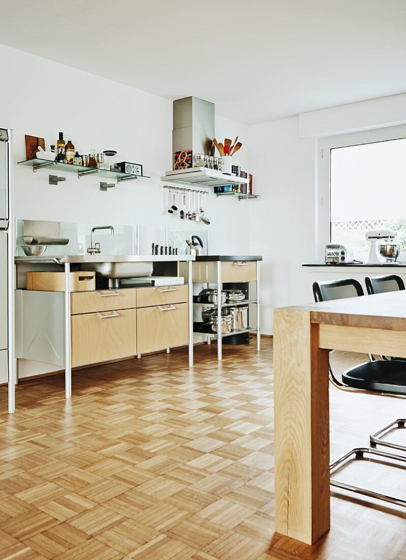 Teilweise sichtbarer Esstisch aus Holz, gegenüber moderne Küchenzeile in minimalistischer Küche