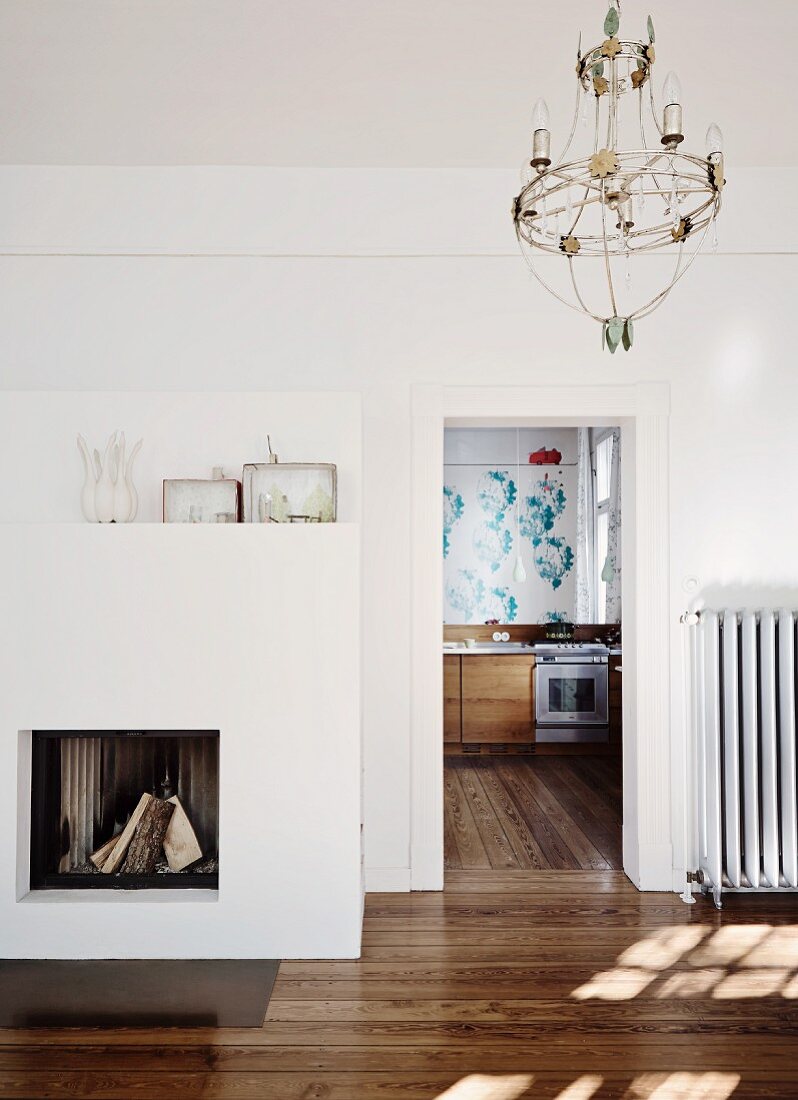 Wohnraum mit Kamin in minimalistischem Ambiente, seitlich offene Tür und Blick in die Küche mit durchgehendem Dielenboden