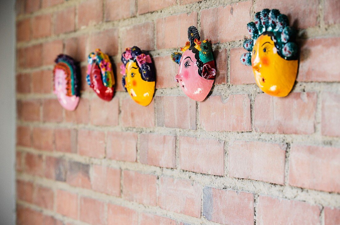 Row of small, painted masks on brick wall