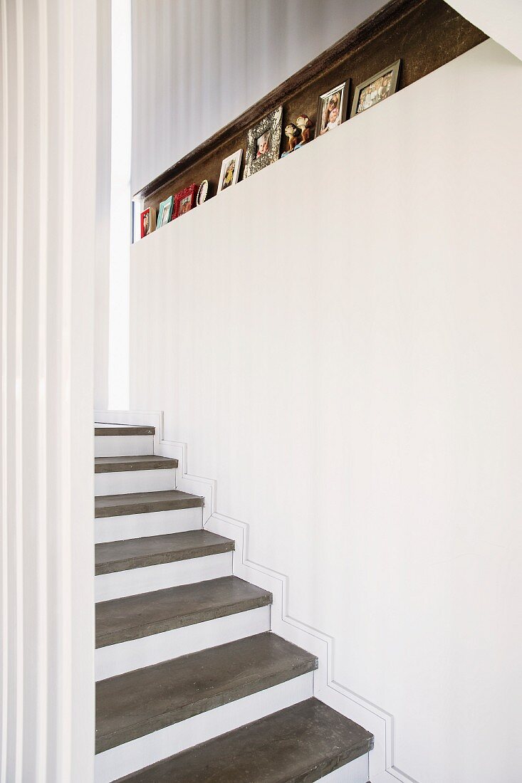 Treppe mit Betontrittstufen auf weißer Setzstufe, in weißer Wand schmale Nische mit gerahmten Fotographien dekoriert