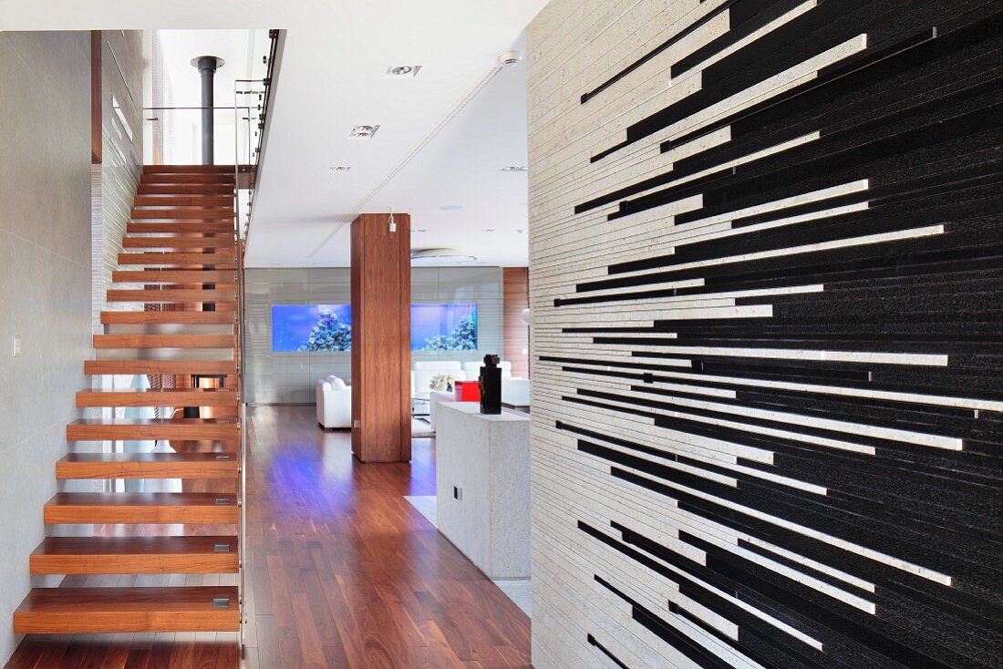 Treppenaufgang mit Massivholzstufen in modernem, offenem Wohnraum, im Vordergrund Raumteiler mit schwarzen und weissen Riemchen-Fliesen
