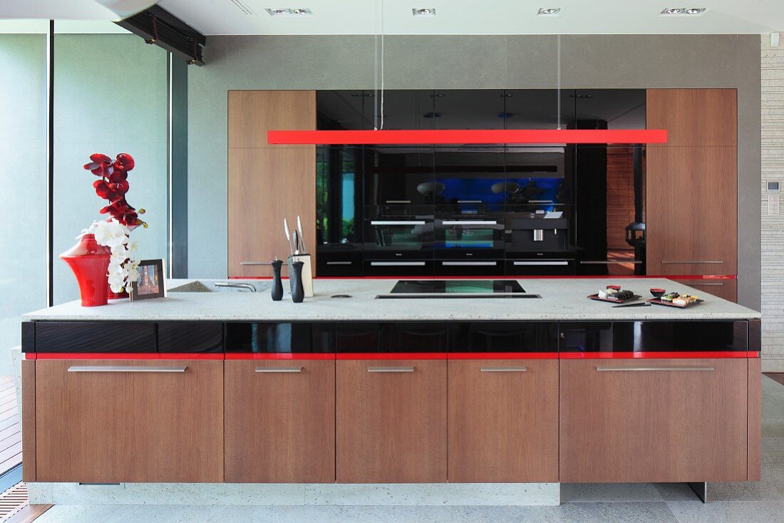 Langer Küchenblock mit Holzunterschränken, darüber Hängeleuchte aus rotlackiertem, stabförmigen Gehäuse in moderner, offener Küche
