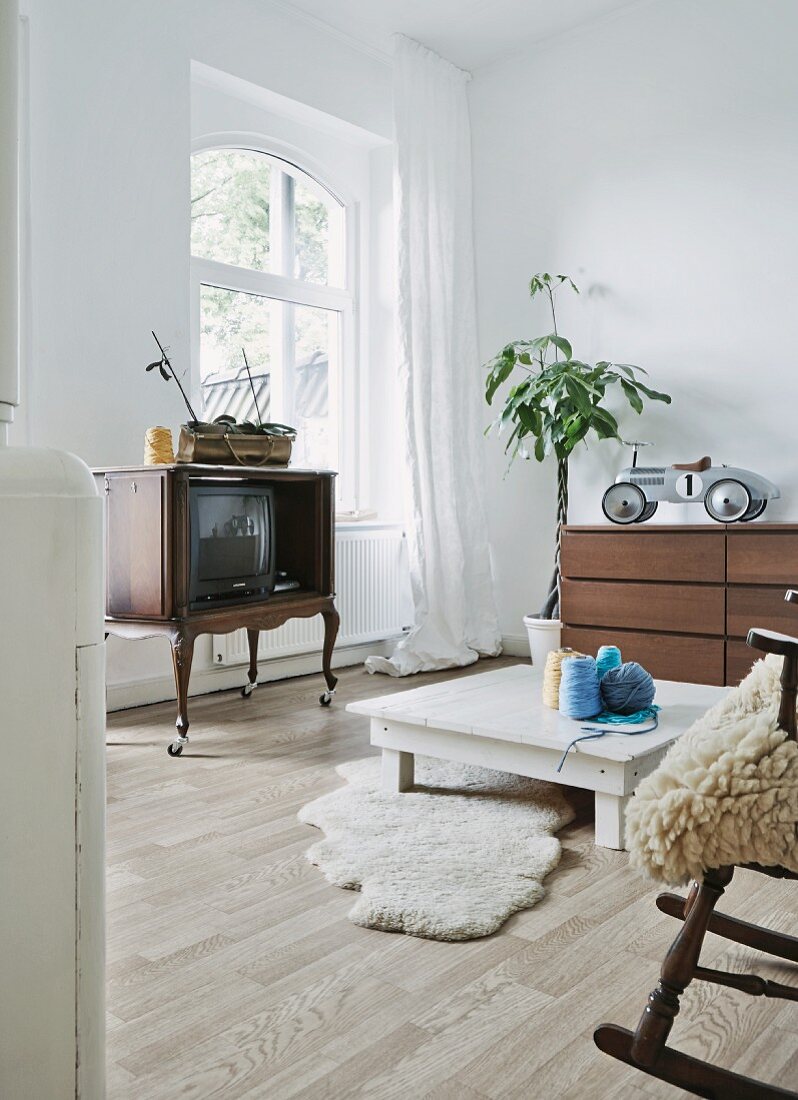 Möbelstilmix in jugendlichem Wohnraum mit Chippendale Fernsehschrank auf Rollen, Schaffellen und Kinderspielauto auf Kommode