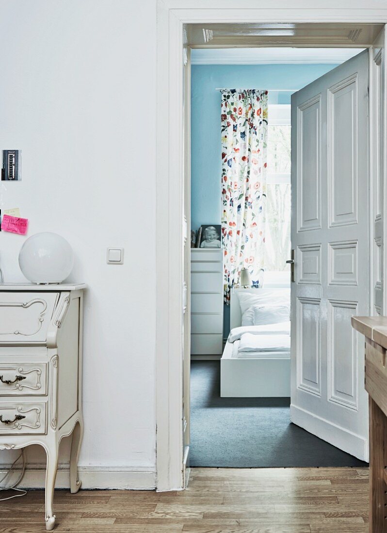 View from corridor with antique bureau into white IKEA bedroom with floor and wall in soft shades of blue